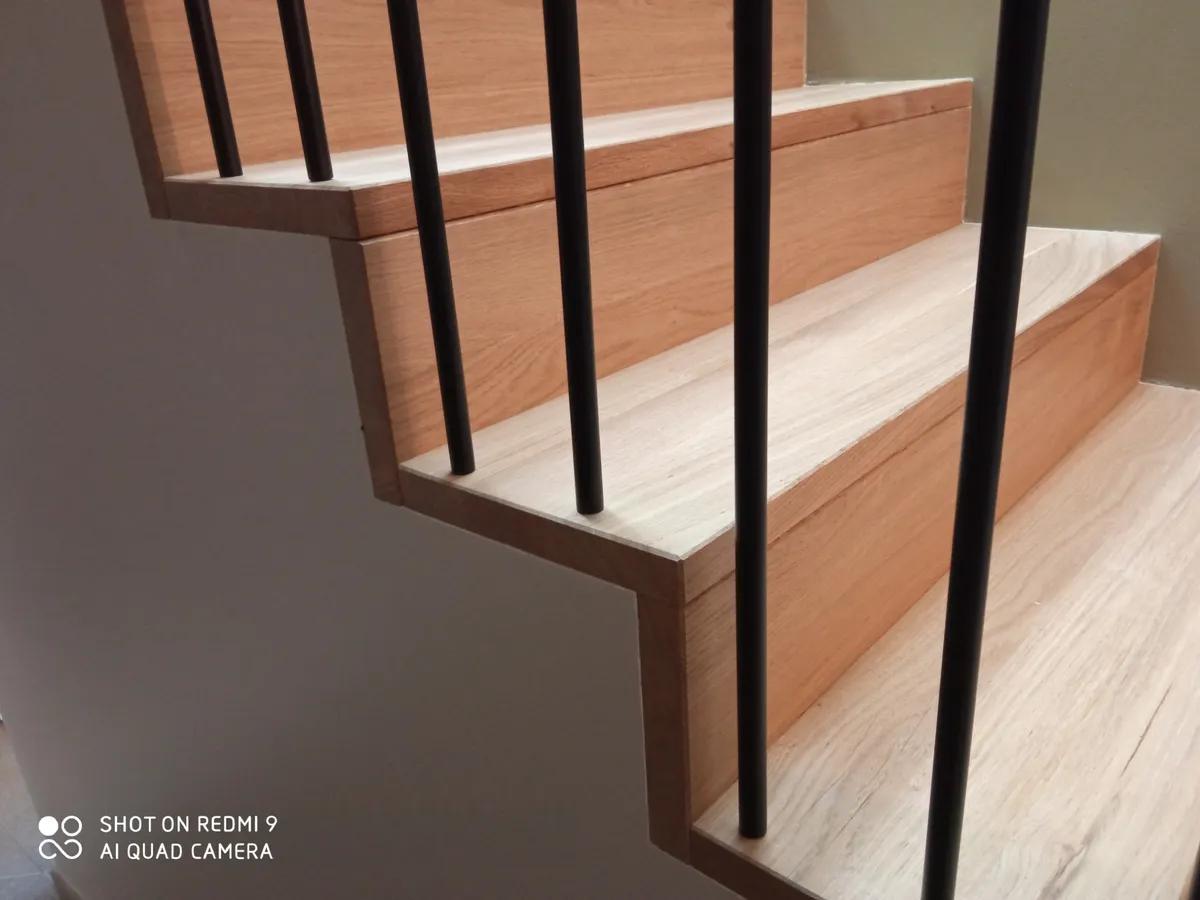Détail d&rsquo;un escalier métallique avec des barres verticales noires et des marches en bois.